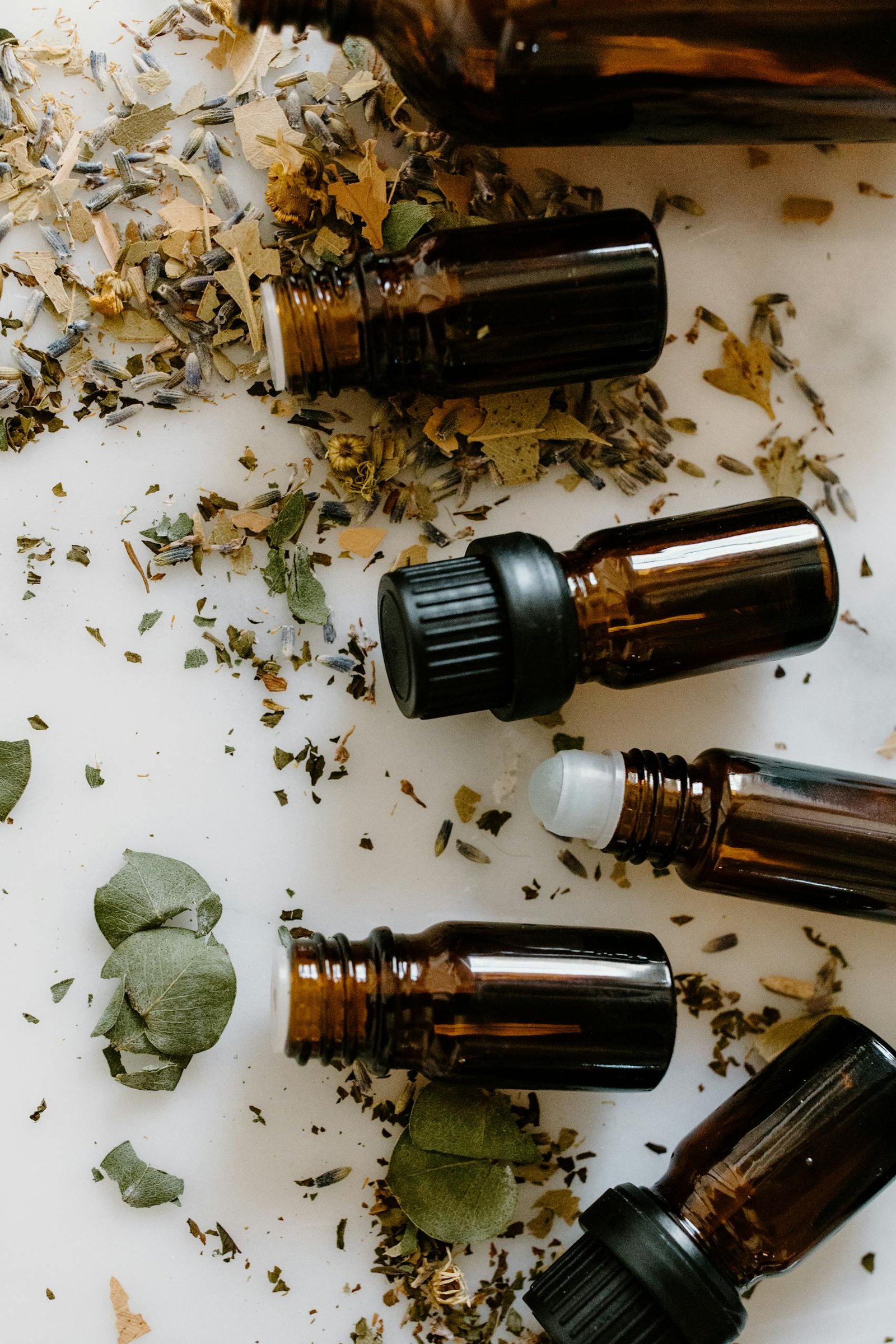 Flat lay of amber glass bottles and dried herbs for aromatherapy on a white surface.