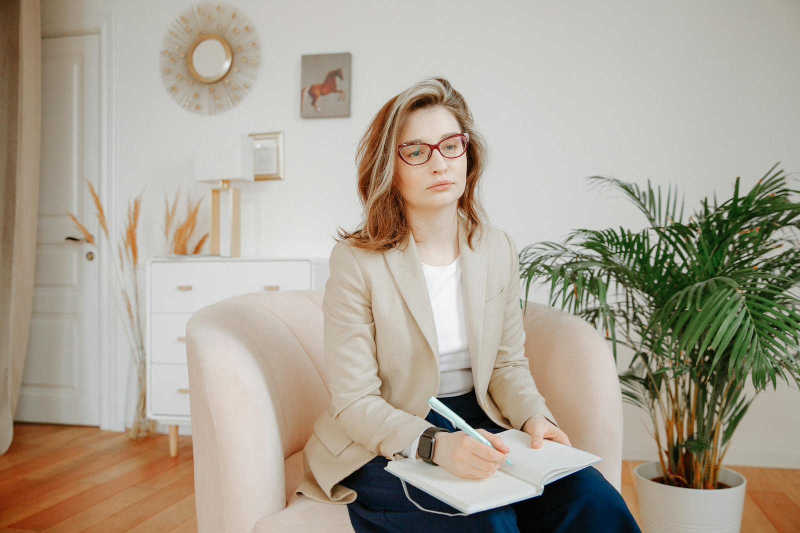 A female therapist in a beige blazer taking notes, focused during a session in a calm office setting.