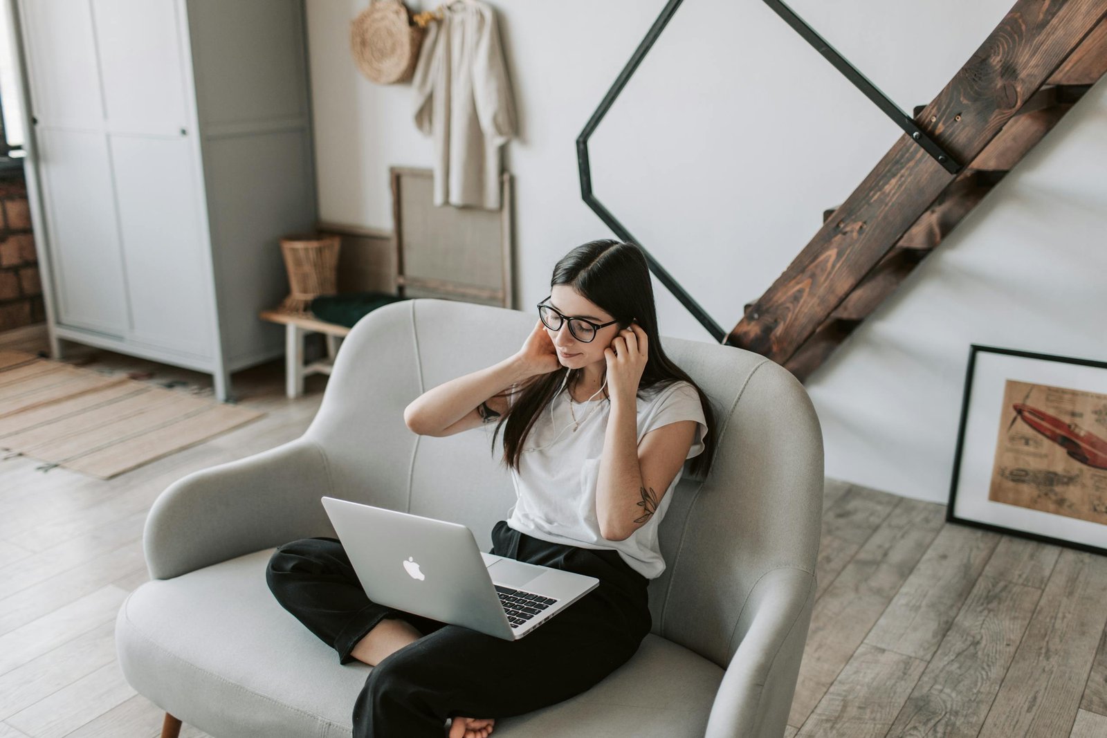 Woman using a laptop on a sofa for a video call. Relaxed home setting with earbuds.