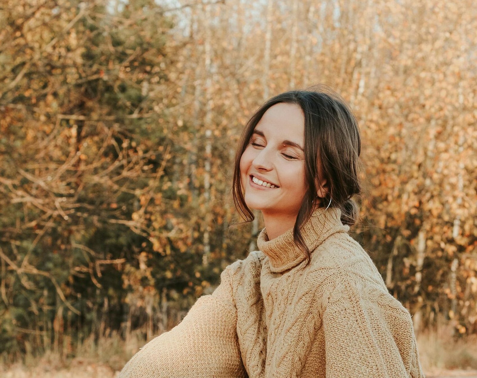 Young woman smiling outdoors in Minsk wearing a cozy beige sweater.