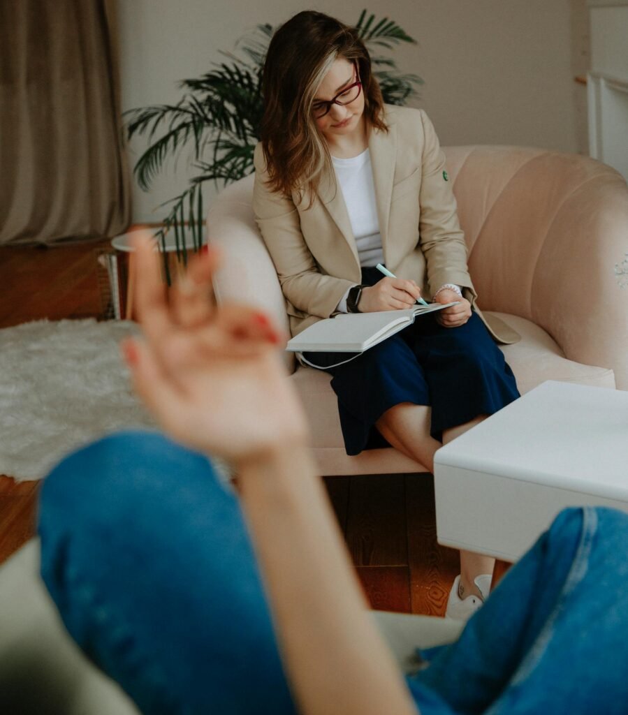 A therapist in a modern office takes notes while listening to a client.