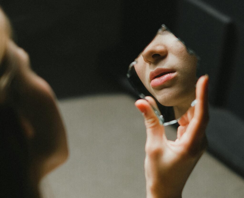 Close-up of a teenage girl holding a broken mirror, her lips reflected indoors.