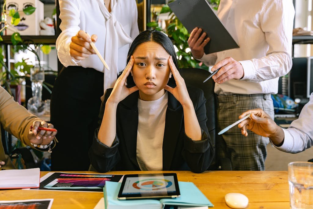 A stressed woman in smart casual attire surrounded by colleagues in an office setting.